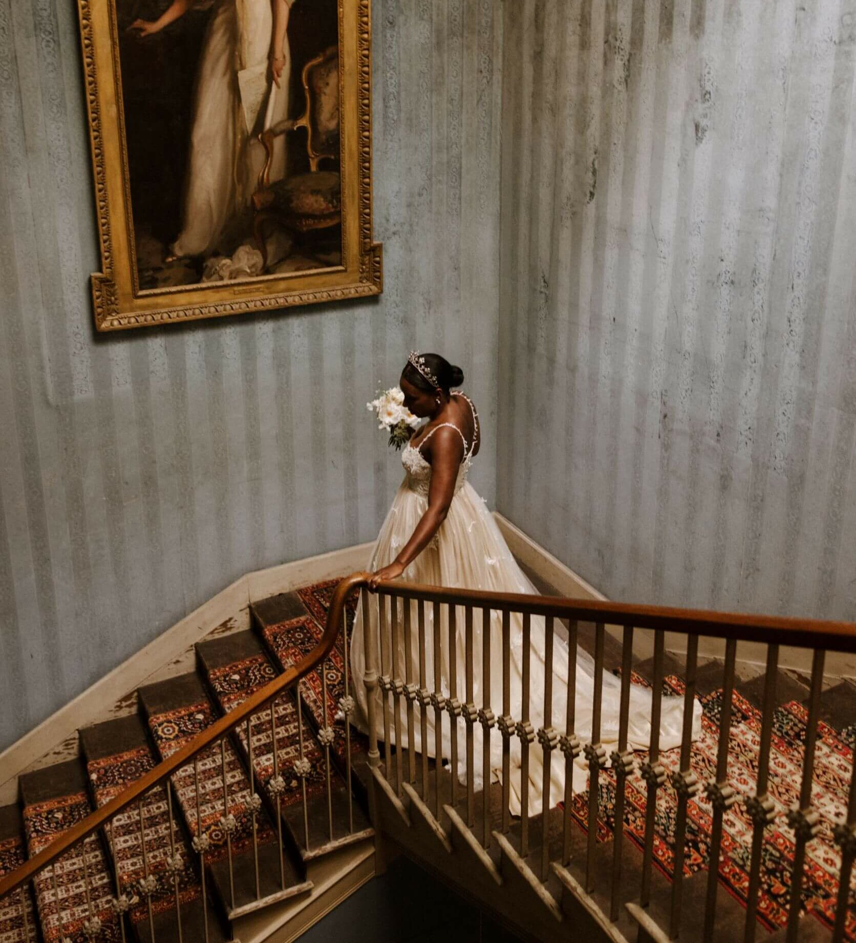 A bride in a custom made gold wedding dress descends a grand stair case to walkdown the aisle