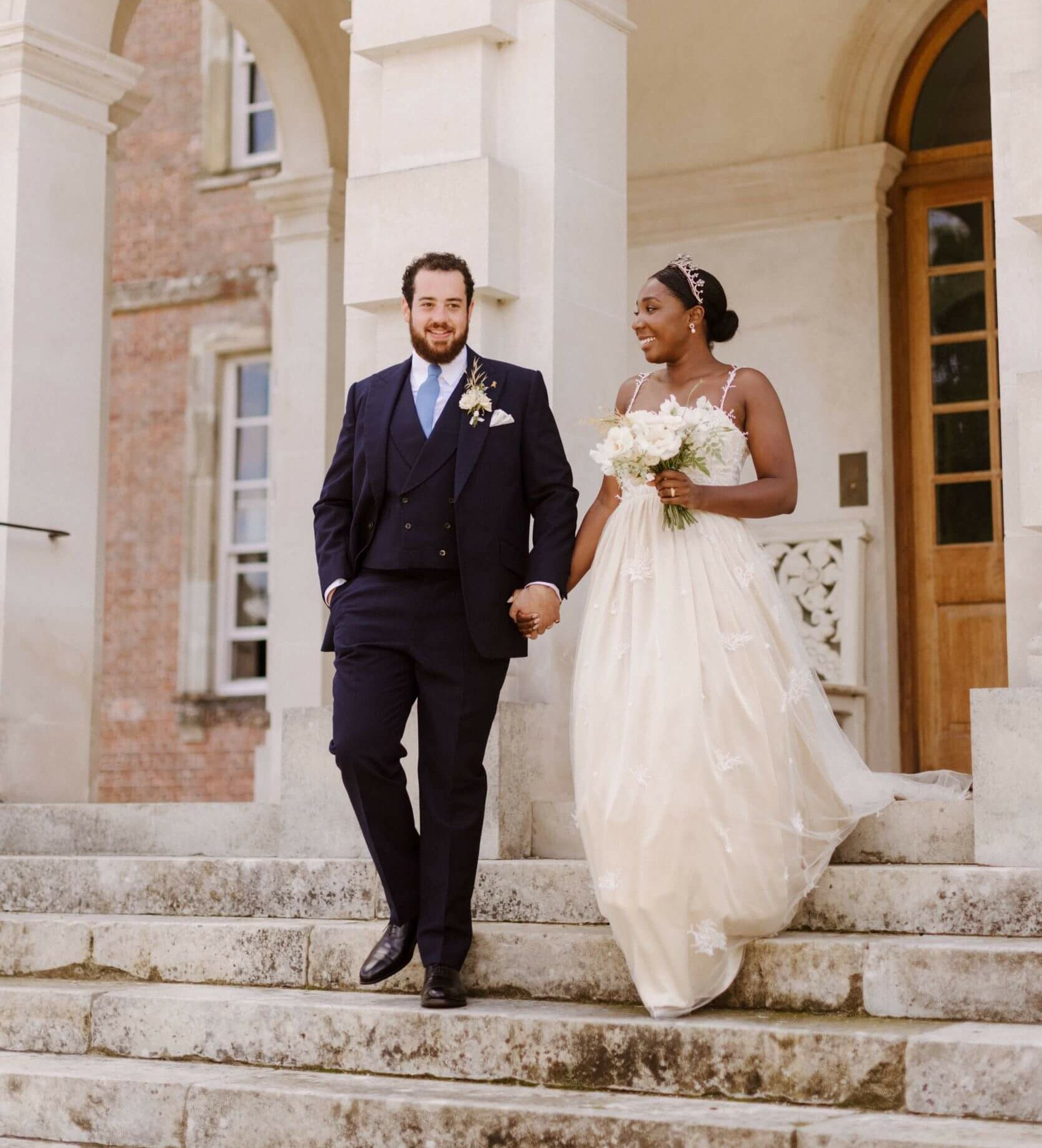 Newly married bride and groom hand in hand on the steps of their wedding venue